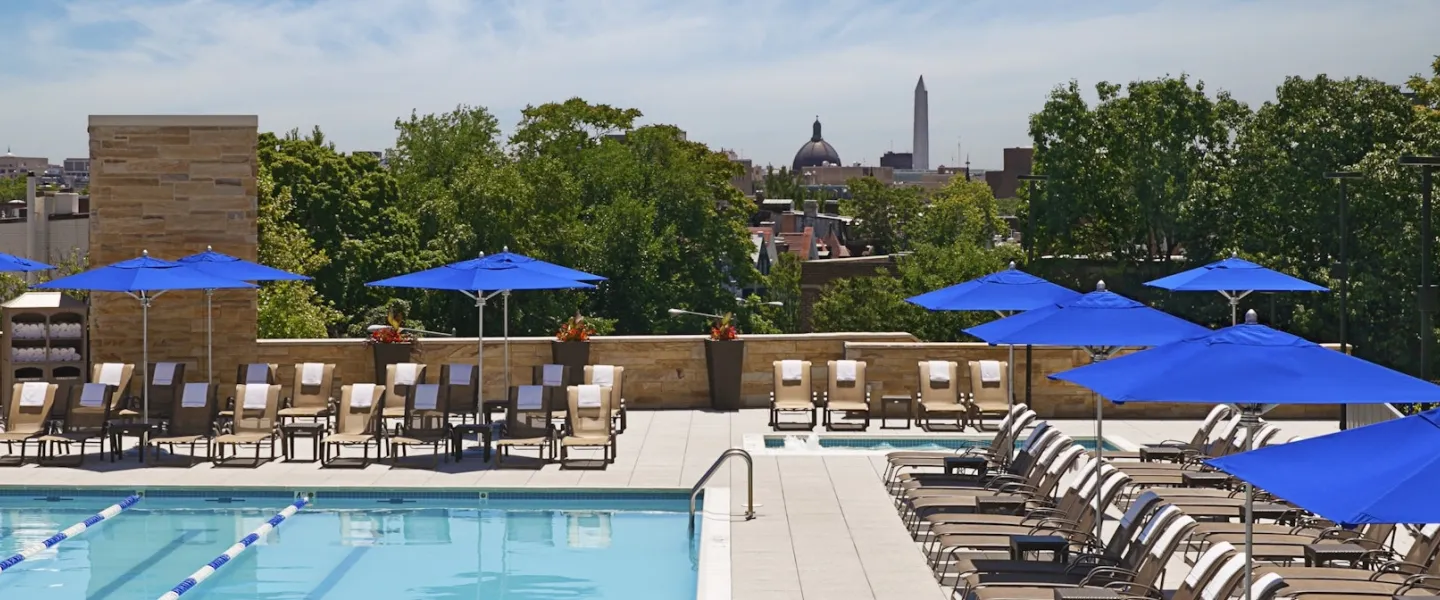 Rooftop pool deck with lounge chairs and blue umbrellas overlooking a city skyline